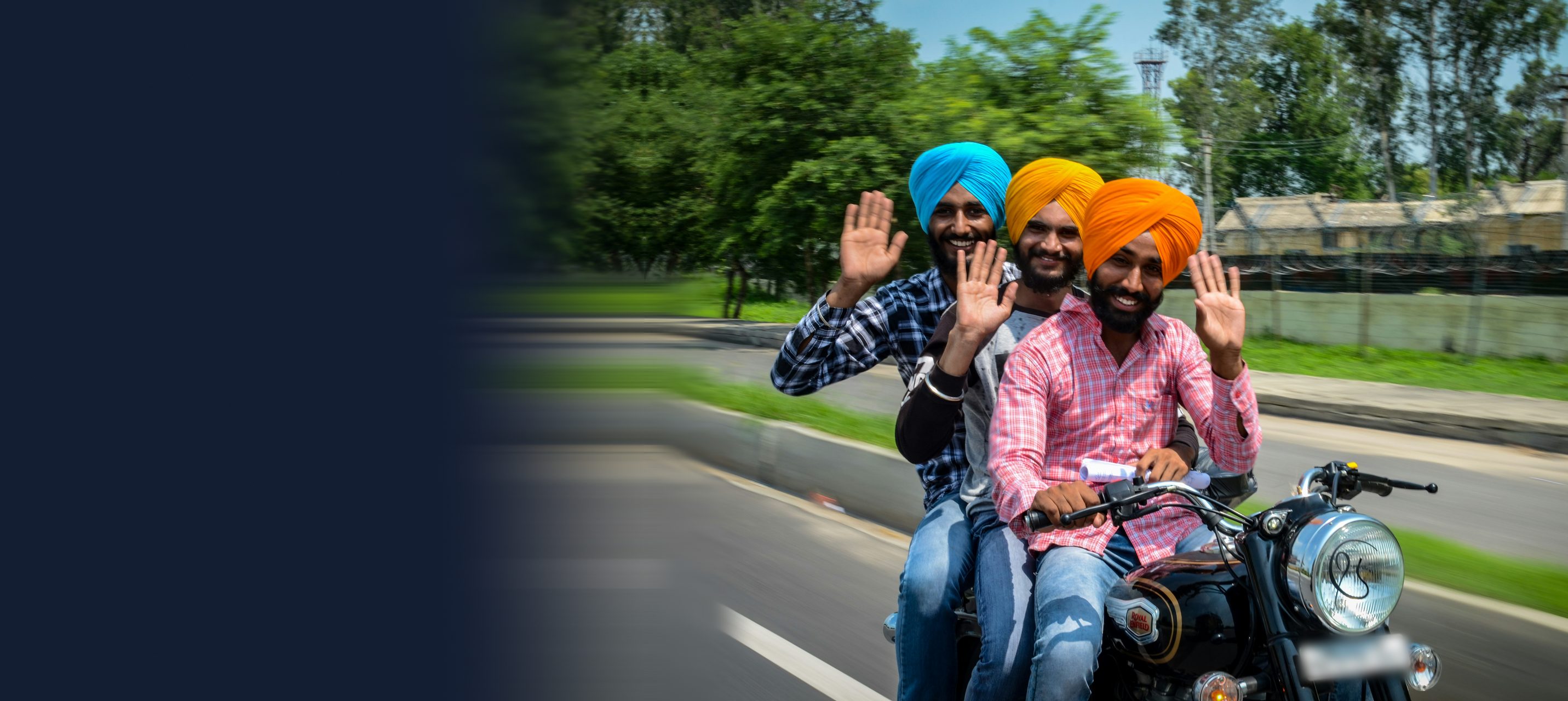 Three young Sardars in sky blue, yellow and saffron turbans, smiling and waving from a motorbike in Punjab