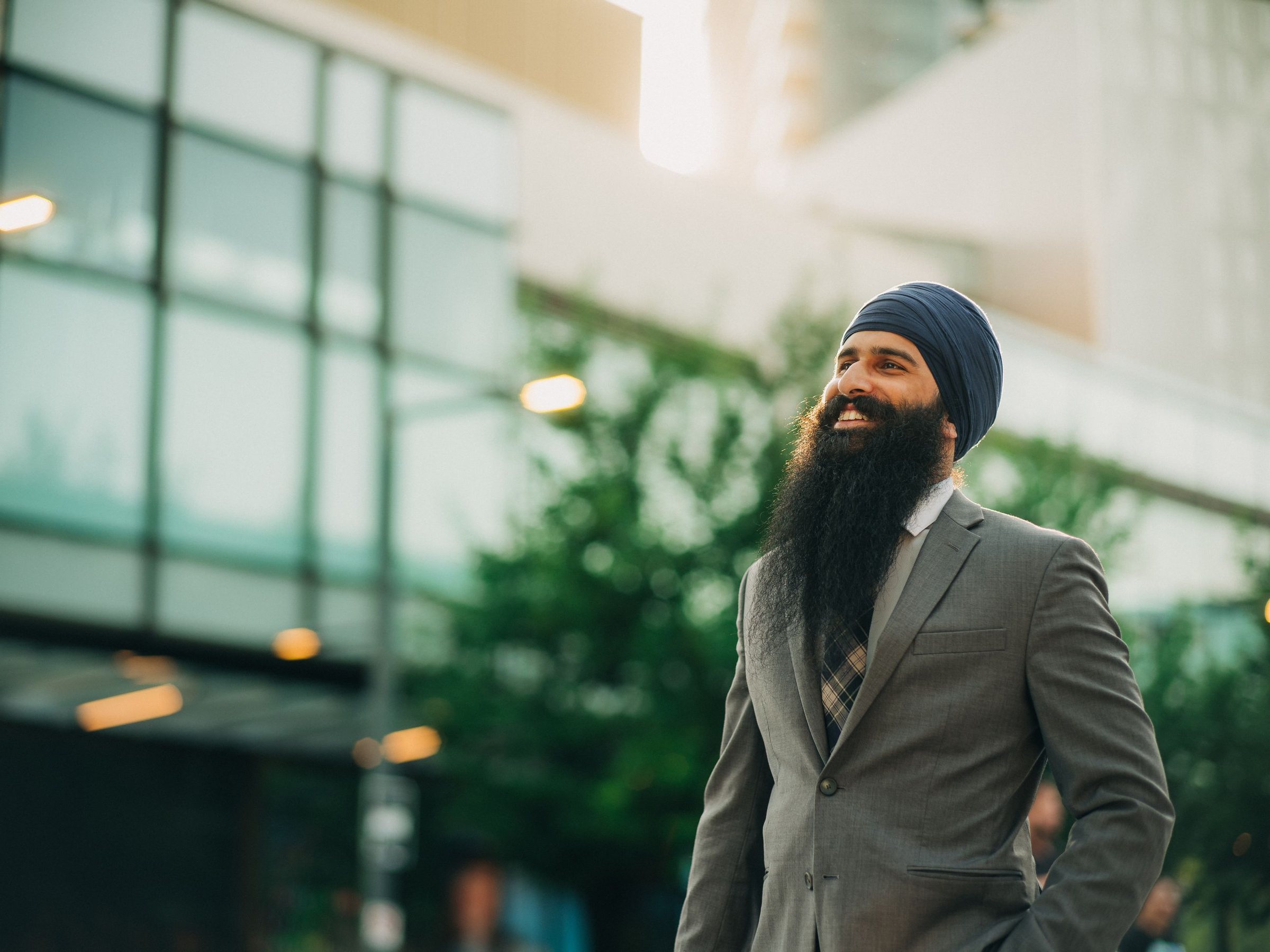 A Sardar in a navy turban and a grey suit, smiling in the city